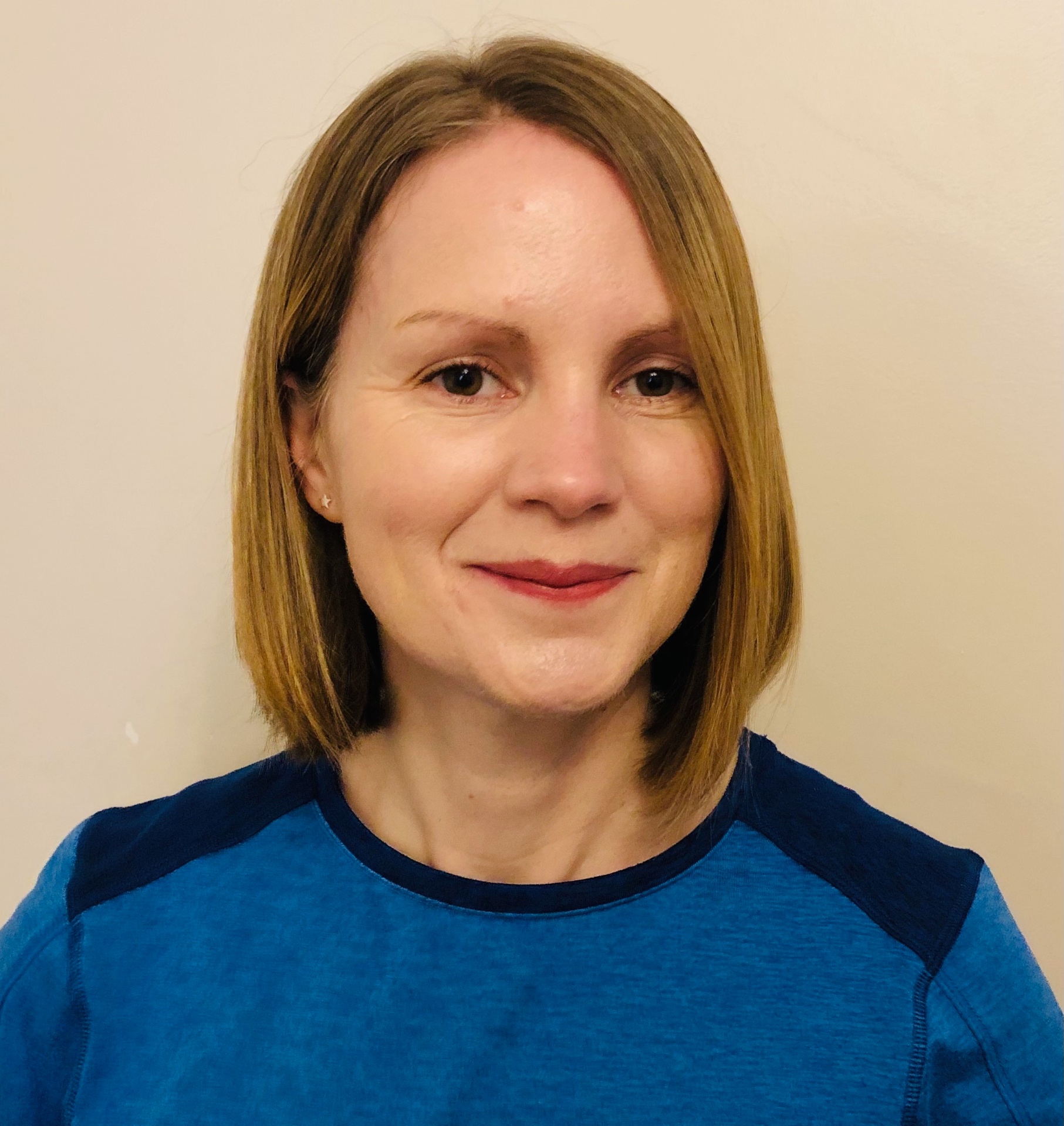 Helen, reformer pilates instructor, smiling with shoulder-length hair in a blue top